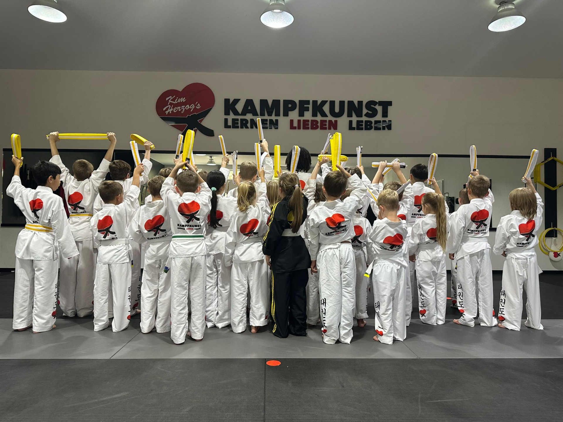 Kinder bei der Gürtelprüfung: sie halten ihre gelben Gürtel in die Höhe